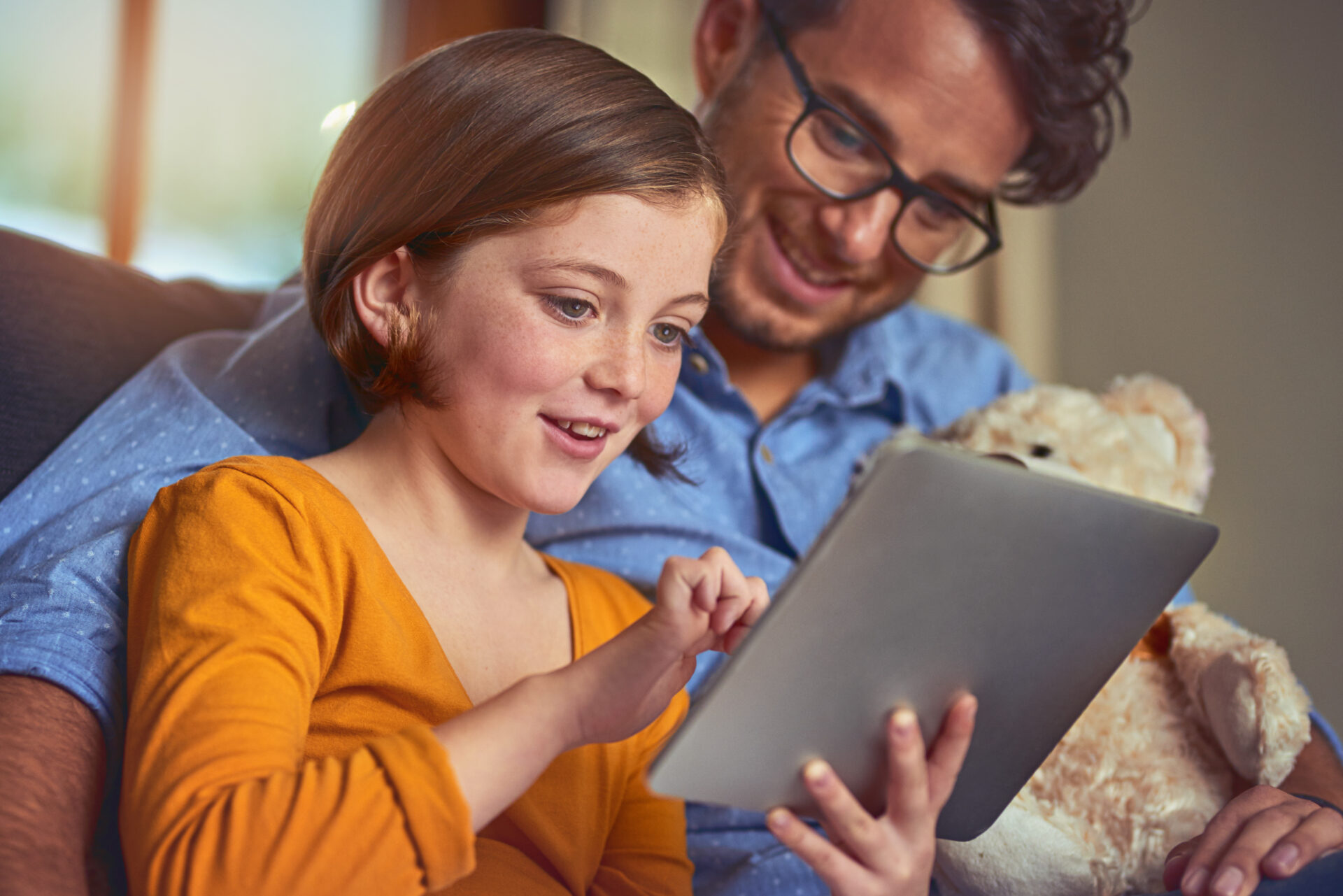 Young person sitting on adult's lap and reading on a tablet.